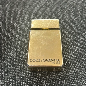Parfym Dolce & Gabbana The One - Säljer en elegant parfym från Dolce & Gabbana, The One. Flaskan är i en lyxig guldton med en fyrkantig form och ett matchande lock. Perfekt för den som vill ha en sofistikerad doftupplevelse.