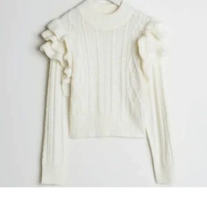 Stickad tröja med volang - Säljer en stilren vit stickad tröja med volangdetaljer på axlarna. Tröjan har en ribbad polokrage och långa ärmar, perfekt för kyligare dagar. Den är både mysig och trendig, ett måste i garderoben! 🤍