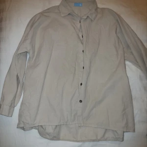 Beige skjorta med knappar - Säljer en stilren beige manchesterskjorta med knappar framtill. Skjortan har en klassisk krage och långa ärmar. Perfekt för en avslappnad look.