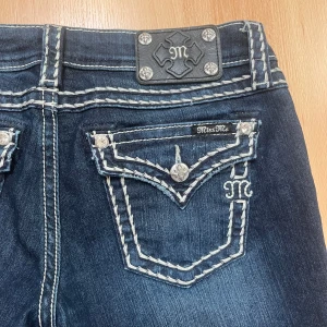 Mörkblå jeans från Miss Me - Snygga mörkblå jeans från Miss Me med dekorativa sömmar och detaljerade bakfickor. Jeansen har en låg midja och är bootcut. Midjemått 29cm. Lite för stora och långa för mig det är därför jag säljer dem. 