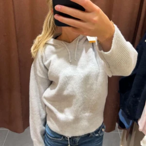 Grå hoodie - Mysig grå hoodie med långa ärmar och dragsko i huvan. Perfekt för en avslappnad stil och passar bra till jeans. Den har en enkel och stilren design som gör den lätt att matcha med andra plagg. Stickad hoodie.