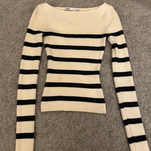 Randig ribbad tröja från Zara - Säljer en snygg ribbad tröja från Zara i beige och svart. Tröjan har ett randigt mönster och långa ärmar. Perfekt för en stilren look! Lite nopprig vid ärmen, annars i bra skick 