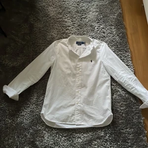 Vit skjorta från Polo Ralph Lauren - Och den är inte gammal typ bara 6 månader. Säljer en klassisk vit skjorta från Polo Ralph Lauren i slim fit. Skjortan har långa ärmar och en broderad logga på bröstet. Perfekt för en stilren look.