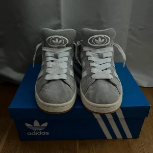 Grå Adidas sneakers - Snygga grå Adidas sneakers med vit snörning och klassiska tre ränder på sidan. Skorna har en stilren design med en bekväm sula och Adidas-logga på plösen och hälen. Säljer då dom är för stora, köpta för 1350kr och säljer för 900kr. Använda ett fåtal gånger men är i mycket bra skick! Du får två helt oanvända gråa snören till skorna i köpet. Perfekta för en avslappnad stil💗