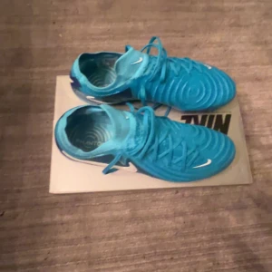 Nike phantom elite  - Snygga blå fotbollsskor från Nike med vit logga och snörning. Skorna har en modern design med mönstrad yta och är perfekta för fotbollsplanen. De kommer med en praktisk förvaringspåse.