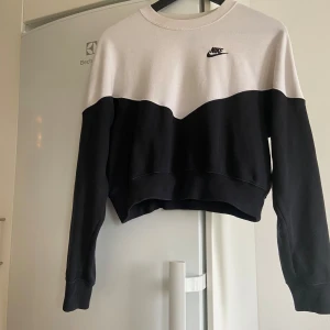 Svart och vit tröja från Nike - Säljer en snygg tröja från Nike i storlek M. Den har en cool tvåfärgad design med Nike-loggan broderad på bröstet. Tröjan är långärmad och har en croppad passform. Tröjan är i använt skick (har en fläck tex vid bröstet, se bild) självklart tvättad. 