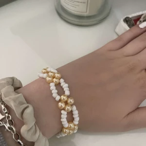 Dubbelradigt pärlarmband i vitt och guld - Säljer ett superfint dubbelradigt armband med vita och guldiga pärlor. Det är justerbart och passar perfekt för både vardag och fest. Armbandet ger en elegant touch till vilken outfit som helst!