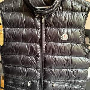 Moncler väst svart, storlek 4 motsvarande L/XL. Västens dragkedja krånglar ibland och ett litet hål på vänster axel (se bild). I övertogs gott skick!