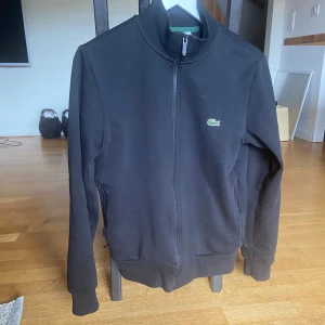 Svart Lacoste tjocktröja - Super fin svart Lacoste tjocktröja storlek S jätte bra skick! Båda fickorna har dragkedja, alla dragkedjor funkar perfekt. Säljer för 850kr.