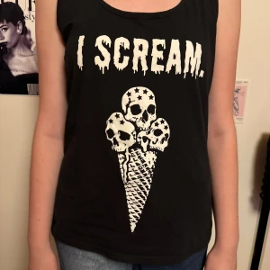 Svart linne med tryck 'I Scream' - Coolt svart linne från emp med trycket 'I Scream' i vit text. Designen har en unik illustration av glass med dödskallar. Perfekt för en avslappnad och edgy stil. Linnet är ärmlöst och gjort i mjukt bomullsmaterial.