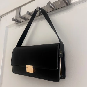 Väska från Ginatricot  - Svart handväska i läder med guld detaljer från Ginatricot. I väskan har du tre fack som du kan se på den sista bilden, mitten facket är med dragkedja. 