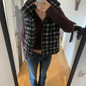 Svart och vit rutig väst med dragkedja - Säljer en superfin svart och vit rutig väst med dragkedja. Den är perfekt för höst och vinter och har en mysig huva. Västen är i normal passform och passar perfekt över en tröja för extra värme🙏🏻