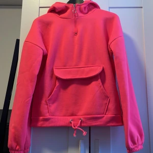 Rosa fleece hoodie - Säljer en supermysig rosa fleece hoodie med dragkedja vid halsen och en stor ficka framtill med knäppning. Den har en justerbar dragsko i nederkanten och långa ärmar med resår vid ärmsluten. Perfekt för kyliga dagar! Oversize