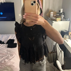Svart blus med volangdetaljer - Säljer en superfin svart blus med volangdetaljer. Den har ett vackert spetsmönster och är perfekt för både vardag och fest. Blusen är ärmlös och har en luftig passform som gör den bekväm att bära. Perfekt att matcha med jeans eller kjol!💗💗