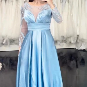 Ljusblå långklänning med spetsdetaljer - Säljer en elegant ljusblå långklänning med vackra spetsdetaljer på ärmarna och överdelen. Klänningen har en v-ringad design och är tillverkad i ett glansigt material som ger en lyxig känsla. Perfekt för bal eller fest!