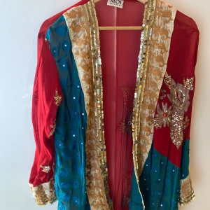 Sagolikt vacker kimono med stenar och broderier  - Magiskt vacker kimono/kavaj i tunn chiffong med guldpaljetter, röda stenar och broderier. Färgerna är varmt rött och grönblått samt gyllene sammet. Handsydd i Indien. Aldrig använd. 