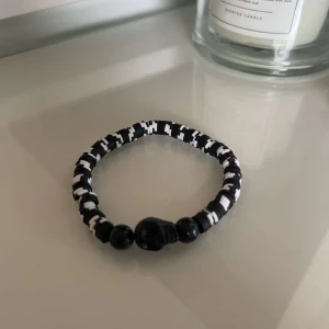 Svartvitt armband med pärlor - Säljer ett coolt svartvitt armband med ett mönster av små pärlor. Armbandet har en elastisk design som gör det lätt att ta på och av. Perfekt för att ge en stilren touch till din outfit!