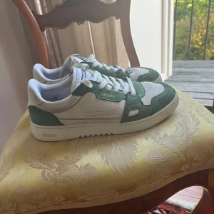 Vita och gröna sneakers från Axel Arigato - Hej! Säljer nu mina Arigato skor då de är för små för mig. De är i bra skick 8/10, men är lite smutsiga i bak. Det är inget man tänker på och är även lätt fixat. Skorna är i storlek 41 men passar 42. Inget og tillkommer. Skriv vid minsta fundering!