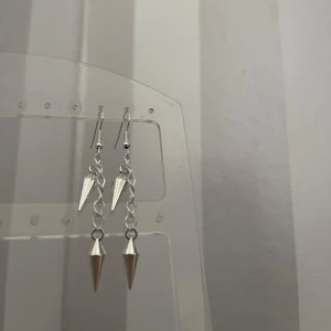 Silvriga örhängen med konformade hängen - Säljer ett par coola silvriga örhängen med nitar. De har en kedjedesign som ger en edgy look och är perfekta för både vardag och fest. Superlätta att bära och matcha med olika outfits! Egengjorda!