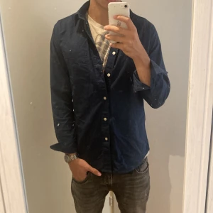Mörkblå skjorta från Selected Homme - Säljer en snygg mörkblå skjorta från Selected Homme. Den är i oxfordstil och har en regular fit xs men passar slim s, perfekt för både vardag och fest. Skjortan är tillverkad av ekologisk bomull och har långa ärmar med knappar. Den är i bra skick och sitter bra på mig som är 180