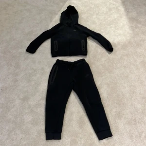 Nike tech set svart i storlek 147-158 CM - Använd några gånger, köpte för 1/2 år sen på JD sports.  Bra skick med inga defekter.  Säljer både tröjan och byxorna i denna annons.  Köpte båda delarna för 2000 kr totalt.  