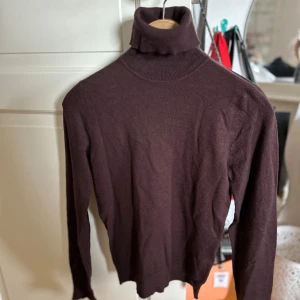 Brun polotröja med knappar - Säljer en snygg brun polotröja med långa ärmar. Tröjan har stiliga knappar vid ärmsluten som ger en extra touch. Perfekt för höst och vinter, och den är supermjuk och bekväm att ha på sig. Passar både till vardags och lite finare tillfällen!