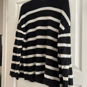 Svart och vit randig stickad tröja - Säljer en supermysig svart och vit randig stickad tröja. Den har långa ärmar och en skön passform som är perfekt för kyliga dagar. Nedtill finns en liten slits på båda sidor. Perfekt för både höst och vinter!