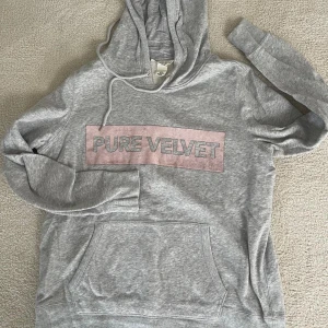 Grå hoodie med texten 'Pure Velvet' - Säljer en supermjuk och bekväm grå hoodie med texten 'Pure Velvet' i rosa på bröstet. Den har en klassisk känguruficka och justerbar huva med dragsko. Perfekt för en avslappnad stil eller mysiga dagar hemma. 🩶