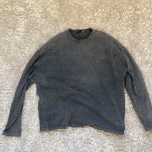 Grå långärmad tröja från ASOS DESIGN - Säljer en grå långärmad tröja från ASOS DESIGN. Den har en cool, tvättad look och ett tryck med texten 'SAINTS' och en blomma på baksidan. Perfekt för en avslappnad stil. Tröjan är i storlek M och är superbekväm att ha på sig.