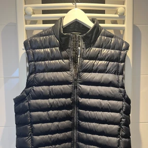  dunväst från J.Lindeberg - Säljer en snygg och stilren marinblå dunväst från J.Lindeberg. Västen har en quiltad design och är perfekt för lager-på-lager under höst och vår. Den har en praktisk dragkedja framtill och är i nyskick. Perfekt för att hålla värmen utan att kompromissa med stilen!