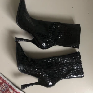 Svarta stövletter med klack och spetsig tå - Säljer ett par snygga svarta klackar med krokodilmönster. Klacken är ca 10 cm. Dem har en dragkedja på sidan för enkel på- och avtagning❤️