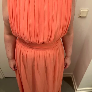 Persikofärgad långklänning med veckad design - Säljer en elegant persikofärgad långklänning med en vacker veckad design från Zetterberg. Klänningens rygg har knappar och en dragkedja för enkel påklädning. Dragkedjan är lite sönder men går fortfarande enkelt att dra upp. Den är uppsydd till en person som är 163 cm. Den är en aning smutsig ned till och är i stl 42/44. Köpt för 2500 och säljer för 450 men kan gå ner i pris! Skriv för övriga frågor🩵