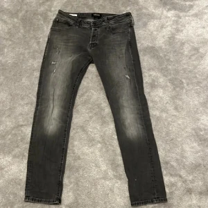 Grå jeans från Jack & Jones - Snygga grå jeans från Jack & Jones med en slim passform. De har en klassisk femficksdesign och en diskret slitning för en trendig look. Perfekta för en avslappnad stil. Tar emot byte 