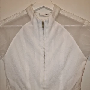 Vit jacka från Fade to W - Snygg tunn jacka från Fade to W med transparenta ärmar. Perfekt för en stilren look med en touch av elegans. Toppen har en modern design som passar till många olika tillfällen. Tvättad 1 gång endast.