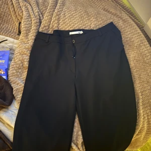 Svarta kostymbyxor - Snygga svarta kostymbyxor med en klassisk design. De har en rak passform och stängs med knapp och dragkedja. Perfekta för en stilren look.