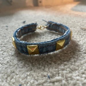 Jeansarmband med gulddetaljer - Snyggt armband i jeansmaterial med fyrkantiga guldfärgade nitar. Storlek: s