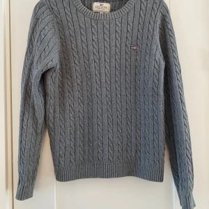 Grå kabelstickad tröja från Lexington - Säljer en stilren grå kabelstickad tröja från Lexington. Tröjan har en klassisk rund halsringning och ett diskret märke på bröstet. Perfekt för kyliga dagar och ger en tidlös look. Grå kabelstickad tröja i strl M från Lexington.  Sparsamt använd och i fint begagnat skick.  Mått Över bröstet: ca 51 cm Längd från axeln och ner: ca 57 cm  100% bomull  Kommer från ett djur och rökfritt hem. 