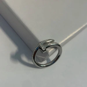 Silverfärgad ring med stenar - Elegant silverfärgad ring med en unik design som liknar en böjd spik. Ringen är dekorerad med små gnistrande stenar längs ena sidan, vilket ger en lyxig känsla. Helt oanvänd, köpt utomlands. Materialet är rostfritt stål.