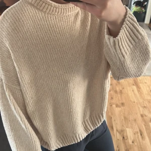 Beige stickad tröja från Pull&Bear - Mysig beige stickad tröja från Pull&Bear med rund hals och långa ärmar. Perfekt för kyligare dagar med sin mjuka och bekväma passform. Tröjan har en ribbad struktur som ger en stilren look.