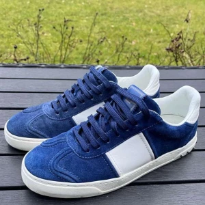 Valentino Flycrew - Snygga blå och vita sneakers från Valentino Garavani i mocka med vita detaljer. Skorna har snörning och små nitar på sidan av sulan för en extra touch. Perfekta för en stilren look. Hör av er vid funderingar!
