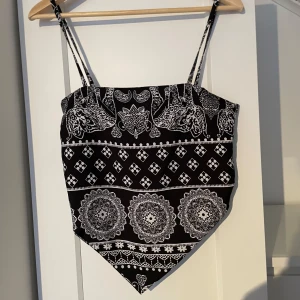 Svart och vit mönstrad bandana-topp - Trendig svart och vit bandana-topp med smala axelband och ett snyggt mönster. Toppen har en knytning bak och en unik design som ger en cool look. Perfekt till sommaren