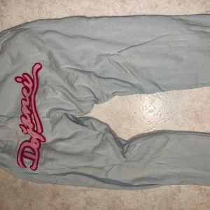 Ljusblå byxor med broderad text grönaktig färg - Snygga ljusblå byxor med en cool broderad text i rött på baksidan. Perfekta för en avslappnad stil. Byxorna har en loose passform och är tillverkade i ett mjukt material för extra komfort.