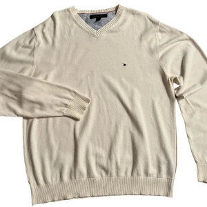 Vit tröja från Tommy Hilfiger - Säljer en stilren vit tröja från Tommy Hilfiger med v-ringning och ribbade muddar. Den har en liten logotyp på bröstet och är perfekt för en avslappnad look.