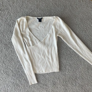 Vit ribbad v-ringad topp - Säljer en stilren vit ribbad topp med v-ringning och långa ärmar. Perfekt för en elegant och avslappnad look.