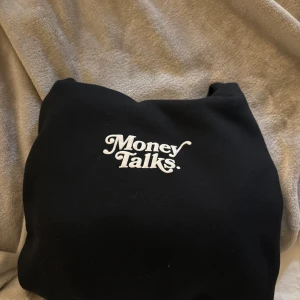 Svart hoodie med texten 'Money Talks' - Säljer en svart hoodie med texten 'Money Talks' tryckt på bröstet. Hoodien har en klassisk design med en stor ficka framtill och en bekväm huva. Perfekt för en avslappnad stil.