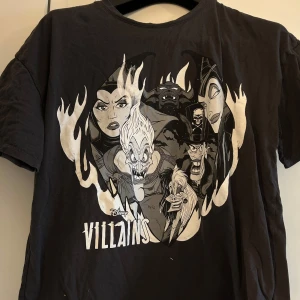 Svart Disney Villains t-shirt - Cool svart t-shirt med tryck av Disney Villains. T-shirten har korta ärmar och ett stort tryck på framsidan med flera kända skurkar från Disney. 