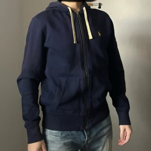 Mörkblå hoodie med dragkedja - Säljer en mörkblå hoodie från Polo Ralph Lauren med dragkedja och justerbar huva. Tröjan har långa ärmar och en liten logotyp på bröstet. Öppen för prisförslag . 