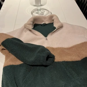Flerfärgad fleece från Zara - Mysig flerfärgad fodrad fleece med fickor från Zara med dragkedja. Tröjan har en hög krage och är perfekt för kyliga dagar. Färgerna är beige, brun och mörkgrön, vilket ger en stilren look.