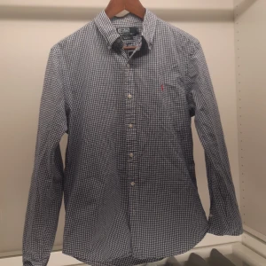 Blårutig skjorta från Ralph Lauren - Snygg blårutig skjorta från Ralph Lauren i slim fit. Skjortan har långa ärmar och knappar framtill. Den är broderad med det klassiska röda Polo-loggan på bröstet. Perfekt för en stilren look!