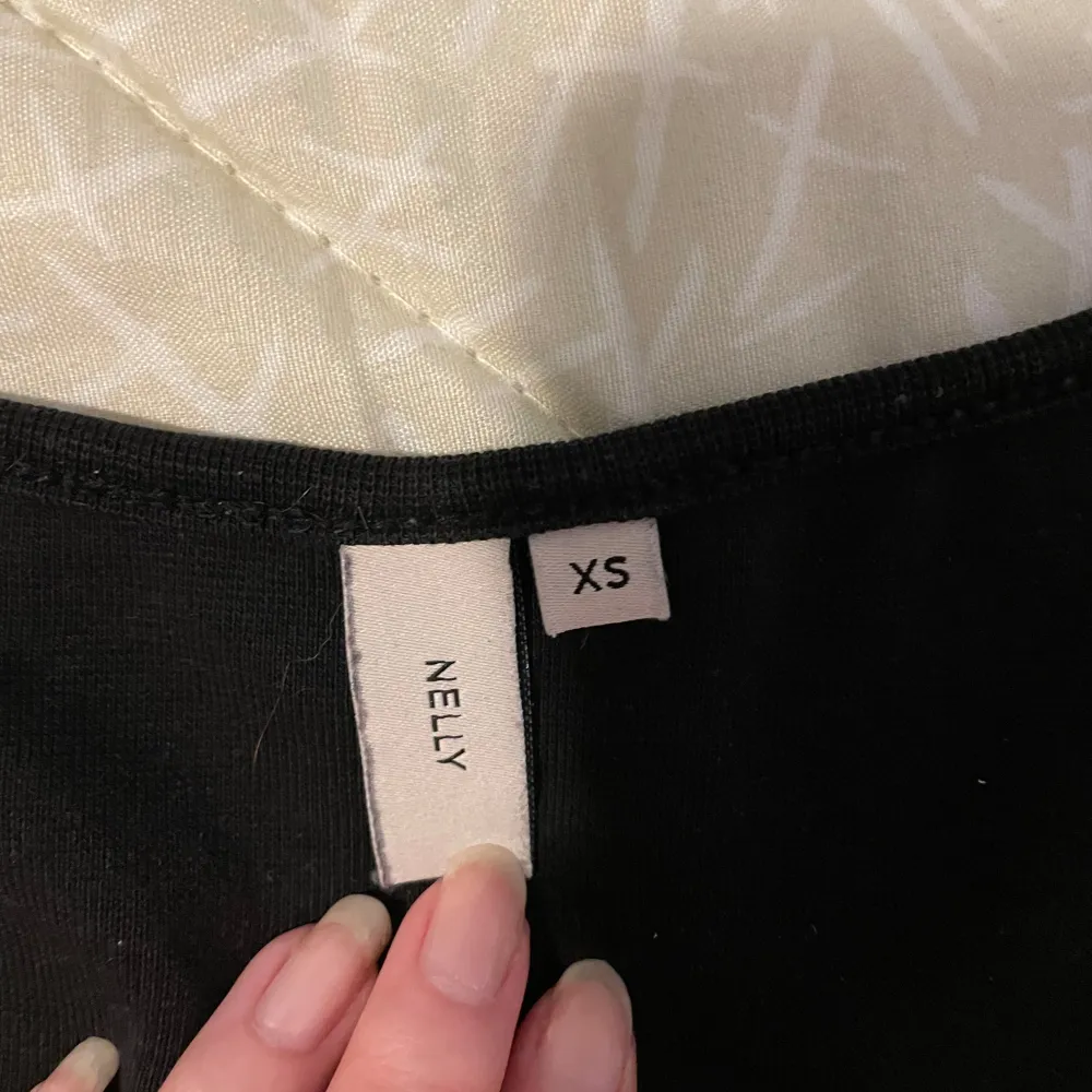 Säljer en stilren svart linnetopp från Nelly i storlek XS. Toppen har en klassisk design med breda axelband och rund halsringning. Perfekt för att matcha med olika outfits.. Yläosat.